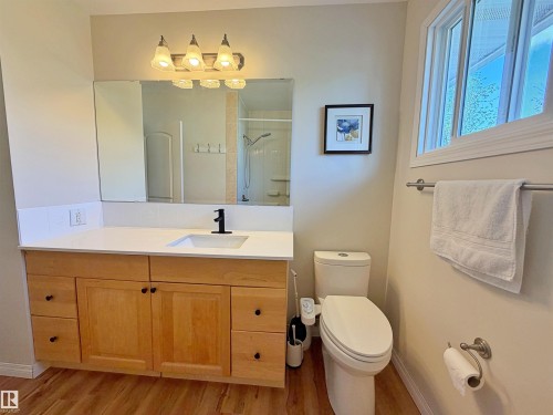 Bathroom featuring a wood-finish vanity with a white countertop, an undermount sink with a matte black faucet, and a large mirror - 9523 151 Street, Edmonton, AB - Indoor Photo Showing Bathroom