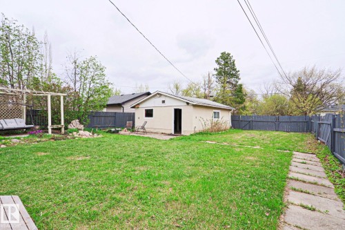 Expansive grassy yard area featuring a detached auxiliary building, perimeter fencing, a wooden pergola structure, and a concrete paver pathway - 9523 151 Street, Edmonton, AB - Outdoor With Backyard