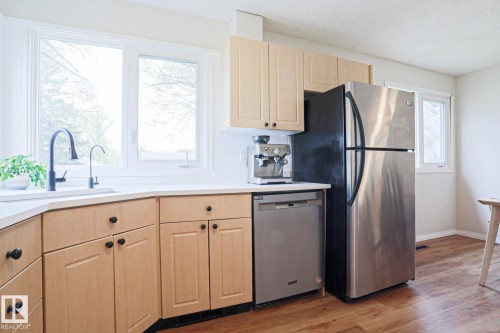 Corner kitchen sink featuring a matte black faucet, light wood-finish cabinetry, light-toned countertops, and a stainless steel refrigerator - 9523 151 Street, Edmonton, AB - Indoor Photo Showing Kitchen