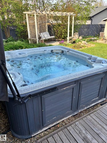 Outdoor spa with a grey textured shell, dark paneling, and a cover lift system, set on a wood-finish deck - 9523 151 Street, Edmonton, AB - Outdoor
