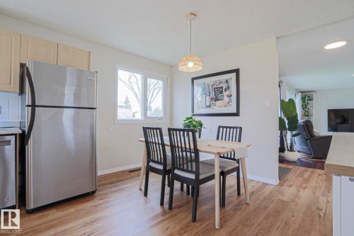 Dining area featuring wood-finish flooring, a double window, light-toned upper cabinetry, stainless steel refrigerator, and a decorative pendant light fixture - 9523 151 Street, Edmonton, AB - Indoor
