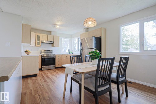 Open-concept kitchen and dining area featuring wood-finish flooring, light wood cabinetry, stainless steel appliances, and white countertops - 9523 151 Street, Edmonton, AB - Indoor