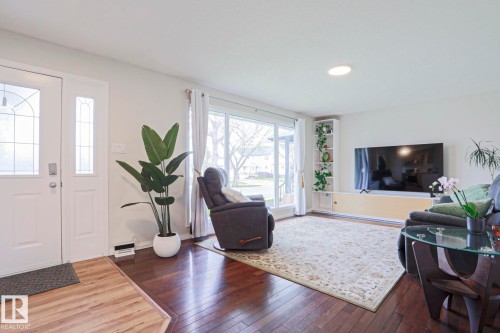 Inviting living space featuring rich wood-finish flooring, a large picture window, a white entry door with decorative glass inserts, and recessed ceiling lighting - 9523 151 Street, Edmonton, AB - Indoor Photo Showing Living Room