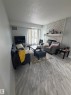 Living area featuring light-toned wood-finish flooring, a white brick-patterned fireplace with a mantel, and a sliding glass door - 205 10136 160 Street, Edmonton, AB  - Indoor Photo Showing Living Room With Fireplace 