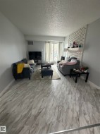Spacious living area featuring light-toned wood-finish flooring and a white painted brick accent wall - 