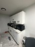 Kitchenette featuring white cabinetry with black hardware, a countertop with a marble-effect finish, a stainless steel sink, and light-colored flooring - 205 10136 160 Street, Edmonton, AB  - Indoor Photo Showing Kitchen 