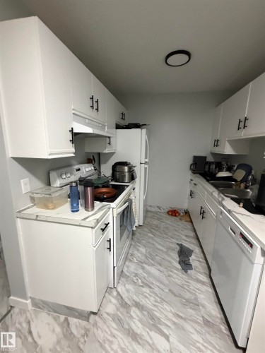 Galley kitchen featuring white cabinetry with black hardware, light-toned countertops, and wood-finish flooring - 205 10136 160 Street, Edmonton, AB - Indoor Photo Showing Kitchen