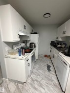 Galley kitchen featuring white cabinetry with black hardware, light-toned countertops, and wood-finish flooring - 