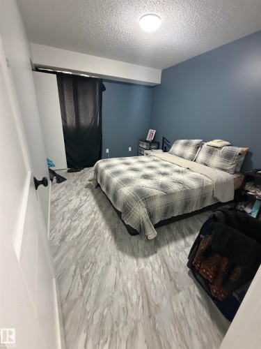 Spacious room featuring light wood-finish flooring, a ceiling-mounted light fixture, and a deep blue accent wall - 205 10136 160 Street, Edmonton, AB - Indoor Photo Showing Bedroom