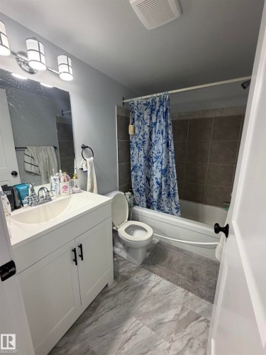 Contemporary bathroom featuring a white vanity with integrated sink, rectangular mirror, and three-light vanity bar - 205 10136 160 Street, Edmonton, AB - Indoor Photo Showing Bathroom