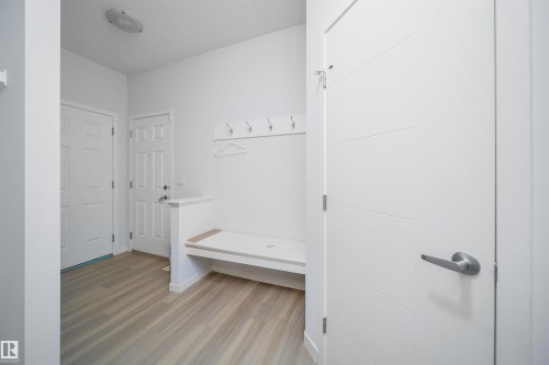 Entryway featuring light wood-finish flooring, a built-in bench, wall-mounted coat hooks, and a contemporary white door with horizontal paneling - 9651 229 Street, Edmonton, AB - Indoor
