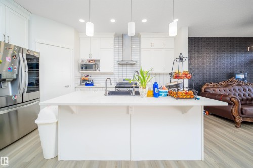 Kitchen featuring a large central island with solid surface countertop, white cabinetry, stainless steel appliances, and a subway tile backsplash - 9651 229 Street, Edmonton, AB - Indoor Photo Showing Kitchen With Upgraded Kitchen