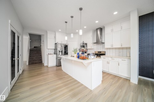 Modern kitchen featuring a large central island, white cabinetry, stainless steel appliances, and wood-finish flooring - 9651 229 Street, Edmonton, AB - Indoor Photo Showing Kitchen With Upgraded Kitchen