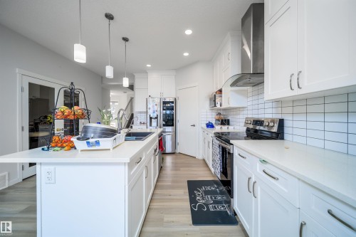 Contemporary kitchen featuring a large central island with an integrated sink, white cabinetry, light countertops, subway tile backsplash, and stainless steel appliances - 9651 229 Street, Edmonton, AB - Indoor Photo Showing Kitchen With Double Sink With Upgraded Kitchen
