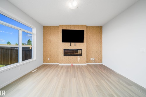 Bright interior space featuring a floor-to-ceiling accent wall with a built-in linear fireplace, wood-finish flooring, and a large multi-pane window - 9651 229 Street, Edmonton, AB - Indoor With Fireplace