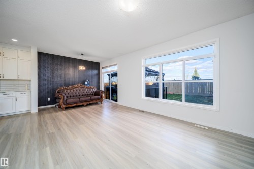 Spacious interior featuring light wood-finish flooring, a large window, white cabinetry with a tile backsplash, and a sliding glass door - 9651 229 Street, Edmonton, AB - Indoor Photo Showing Living Room