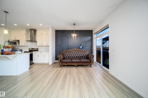 Open-concept living area featuring light wood-finish flooring, a contemporary kitchen with white cabinetry, a subway tile backsplash, and stainless steel appliances - 9651 229 Street, Edmonton, AB - Indoor