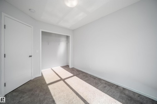 Neutral-toned carpet flooring in a spacious room featuring a flush-mount ceiling light fixture, an open closet with wire shelving, and a white interior door - 9651 229 Street, Edmonton, AB - Indoor Photo Showing Other Room