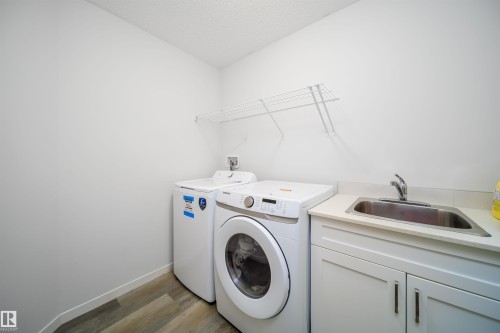 Laundry area featuring wood-finish flooring, white cabinetry, a built-in utility sink, and a wire shelving unit - 9651 229 Street, Edmonton, AB - Indoor Photo Showing Laundry Room