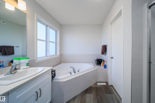 Contemporary bathroom featuring a corner soaking tub, a single vanity with a white countertop and integrated sink, a large mirror, and wood-finish flooring - 9651 229 Street, Edmonton, AB - Indoor Photo Showing Bathroom