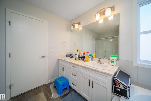 Bathroom featuring a dual-sink vanity with white cabinetry and light-toned countertops, a large framed mirror, and integrated vanity lighting - 9651 229 Street, Edmonton, AB - Indoor Photo Showing Bathroom