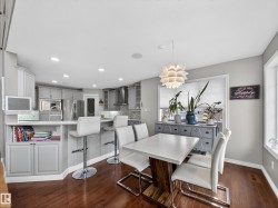 Open-concept kitchen and dining area featuring rich wood-finish flooring, light grey cabinetry, stainless steel appliances, and recessed lighting - 