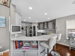 Contemporary kitchen featuring light gray cabinetry, stainless steel appliances, a mosaic tile backsplash, and a breakfast bar with a quartz countertop - 