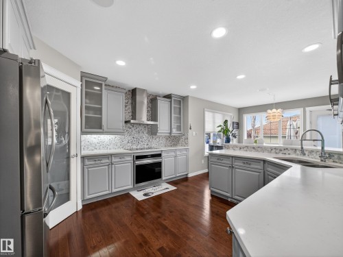 Kitchen featuring gray cabinetry, stainless steel appliances, a tile backsplash, light countertops, and wood-finish flooring - 1062 Tory Road, Edmonton, AB - Indoor Photo Showing Kitchen With Upgraded Kitchen