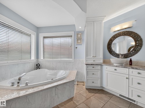 Soaking tub with a polished chrome faucet, surrounded by marble-finish tile and a stone-finish deck - 1062 Tory Road, Edmonton, AB - Indoor Photo Showing Bathroom
