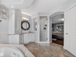 Spacious bathroom featuring a corner soaking tub with mosaic tile surround, a glass-enclosed shower with tiled walls, and a vanity with a vessel sink and abundant white cabinetry - 