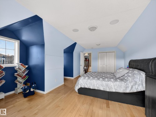 Attic room featuring light wood-finish flooring, a window with exterior views, built-in ceiling speakers, and double bi-fold closet doors - 1062 Tory Road, Edmonton, AB - Indoor Photo Showing Bedroom