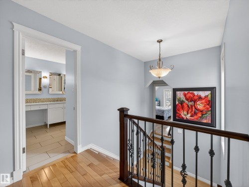 Hardwood flooring extends from the hallway toward a staircase featuring dark wood newel posts and wrought iron balusters - 1062 Tory Road, Edmonton, AB - Indoor Photo Showing Other Room