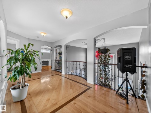 Upper-level hallway featuring wood-finish flooring with decorative inlay, arched doorways, a built-in desk area, and a wrought iron banister overlooking the lower level - 1062 Tory Road, Edmonton, AB - Indoor Photo Showing Other Room