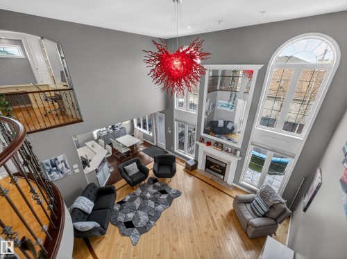 Two-story living area featuring a prominent red art chandelier, hardwood flooring, and a fireplace with a mantel - 1062 Tory Road, Edmonton, AB - Indoor With Fireplace