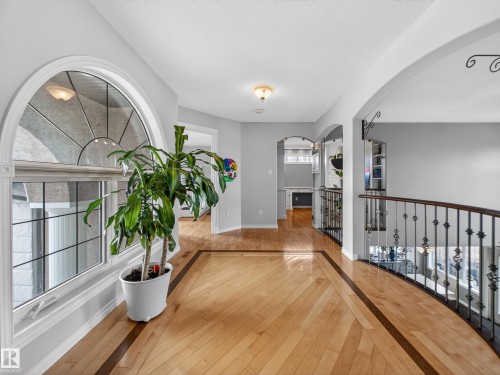 Upper-level landing featuring light wood-finish flooring with dark wood-finish inlay, decorative wrought iron railings, an arched window, and ceiling-mounted light fixtures - 1062 Tory Road, Edmonton, AB - Indoor Photo Showing Other Room