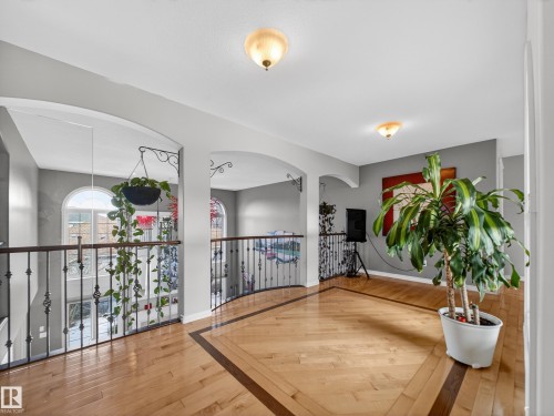 Expansive upper landing featuring wood-finish flooring with a decorative inlay, wrought iron railings, arched architectural details, and recessed lighting - 1062 Tory Road, Edmonton, AB - Indoor Photo Showing Other Room