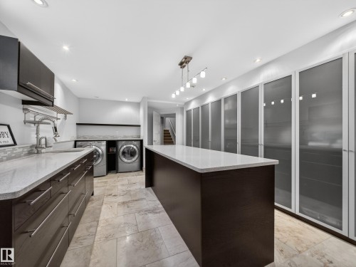 Spacious utility area featuring extensive custom cabinetry, a large center island with a light-toned countertop, a built-in laundry station with side-by-side appliances, a utility sink, and recessed lighting - 1062 Tory Road, Edmonton, AB - Indoor