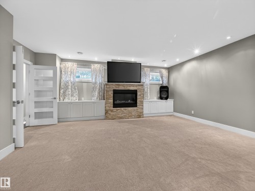 Spacious room featuring a stone-clad fireplace with an electric insert, built-in cabinetry, recessed lighting, and soft pile carpeting - 1062 Tory Road, Edmonton, AB - Indoor With Fireplace