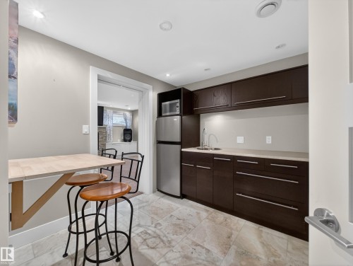 Compact kitchenette featuring dark wood-finish cabinetry, a stainless steel sink with a gooseneck faucet, light-toned countertops, and integrated under-cabinet lighting - 1062 Tory Road, Edmonton, AB - Indoor Photo Showing Kitchen