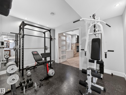 Dedicated exercise room featuring dark rubber flooring, recessed lighting, a full-height wall mirror, and a frosted glass door to an adjacent space - 1062 Tory Road, Edmonton, AB - Indoor Photo Showing Gym Room