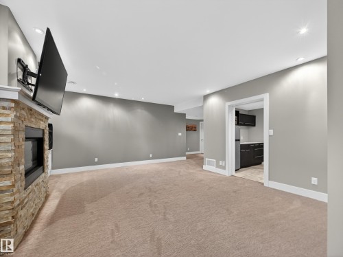 Spacious room featuring a stone-clad fireplace with a built-in television mount, recessed lighting, and soft carpeting - 1062 Tory Road, Edmonton, AB - Indoor Photo Showing Other Room With Fireplace