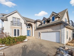Stucco and stone exterior featuring multiple gabled roofs, a prominent arched entry with a blue double door, a two-car garage, and a second-story balcony - 