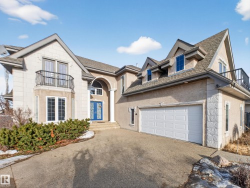 Stucco and stone exterior featuring multiple gabled roofs, a prominent arched entry with a blue double door, a two-car garage, and a second-story balcony - 1062 Tory Road, Edmonton, AB - Outdoor