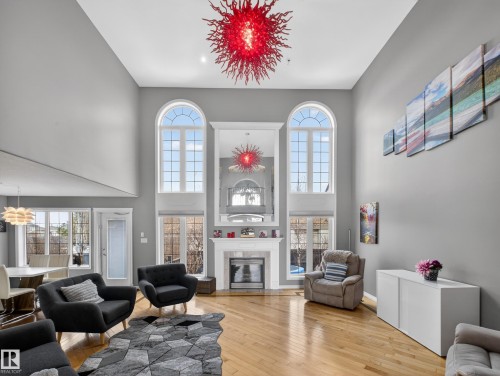 Double-height great room featuring arched windows, a fireplace with a white mantel, and wood-finish flooring - 1062 Tory Road, Edmonton, AB - Indoor Photo Showing Living Room With Fireplace