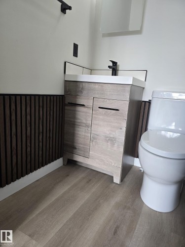 Modern vanity with a light wood-finish cabinet, integrated white sink, and matte black faucet - 11628 151 Avenue, Edmonton, AB - Indoor Photo Showing Bathroom
