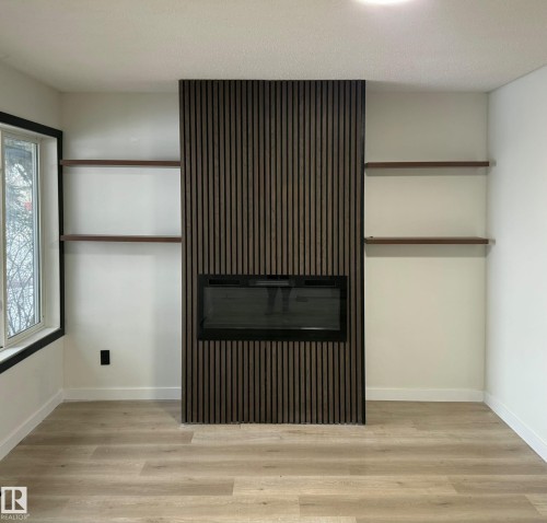 Contemporary linear fireplace set within a dark wood-slat accent wall, flanked by floating wood shelves - 11628 151 Avenue, Edmonton, AB - Indoor Photo Showing Other Room