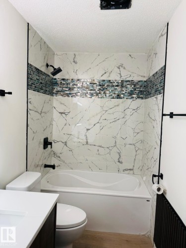 Bathroom featuring a full tub with shower, white marbled wall tiling, and a decorative glass mosaic accent band - 11628 151 Avenue, Edmonton, AB - Indoor Photo Showing Bathroom