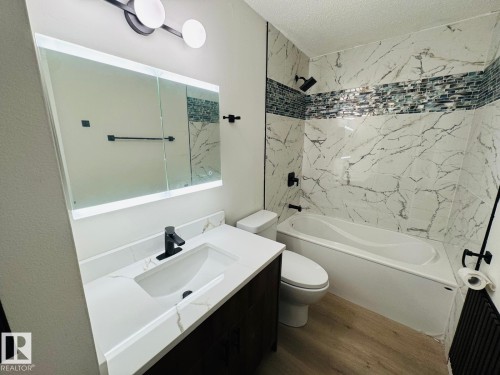 Bathroom featuring wood-finish flooring, a contemporary vanity with a white countertop and undermount sink, and an illuminated mirror - 11628 151 Avenue, Edmonton, AB - Indoor Photo Showing Bathroom