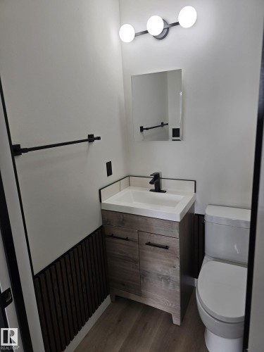 Bathroom featuring a wood-finish vanity with an integrated sink, matte black faucet, and modern spherical lighting fixture - 11628 151 Avenue, Edmonton, AB - Indoor Photo Showing Bathroom