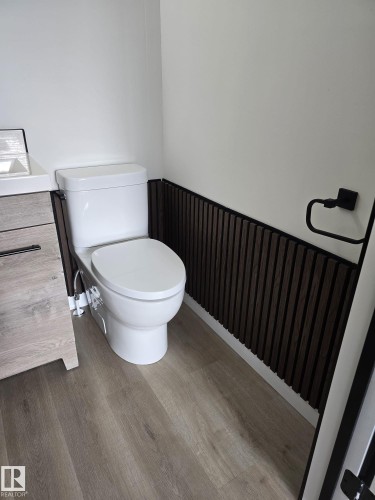 Contemporary powder room featuring a white toilet, dark wood-finish slat wall paneling, and a light wood-finish vanity - 11628 151 Avenue, Edmonton, AB - Indoor Photo Showing Bathroom